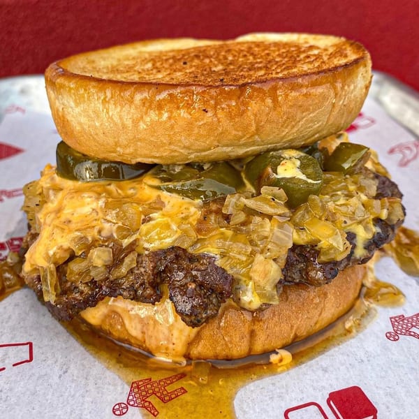 Close-up of a messy burger with cheese, onions, and jalapeños on a toasted bun.