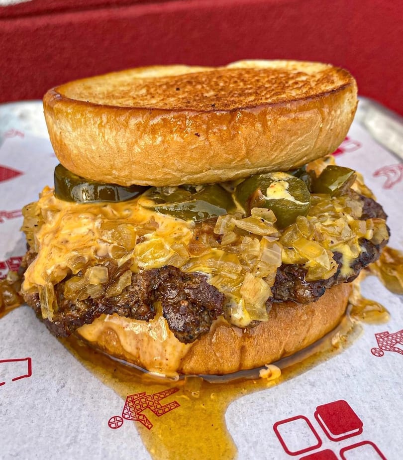 Close-up of a messy burger with cheese, onions, and jalapeños on a toasted bun.