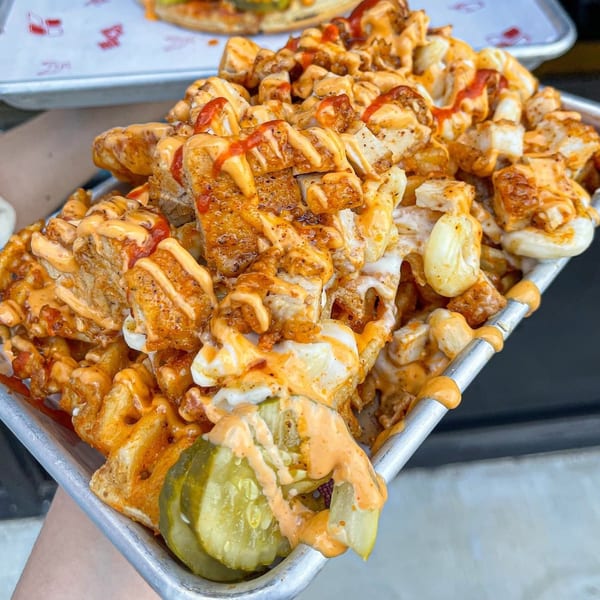 Loaded waffle fries with crispy chicken, melted cheese, and spicy sauces, served with pickles.
