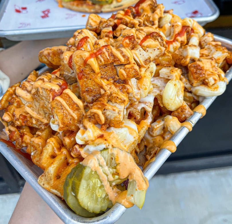 Loaded waffle fries with crispy chicken, melted cheese, and spicy sauces, served with pickles.