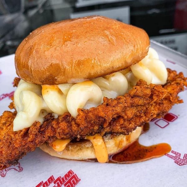 Fried chicken sandwich topped with creamy mac and cheese and spicy sauce on a brioche bun.