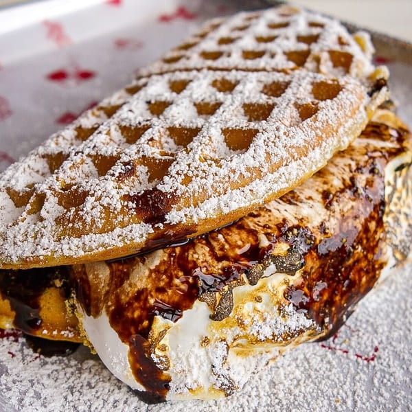 Golden waffle sandwich with gooey toasted marshmallow, chocolate drizzle, and powdered sugar.