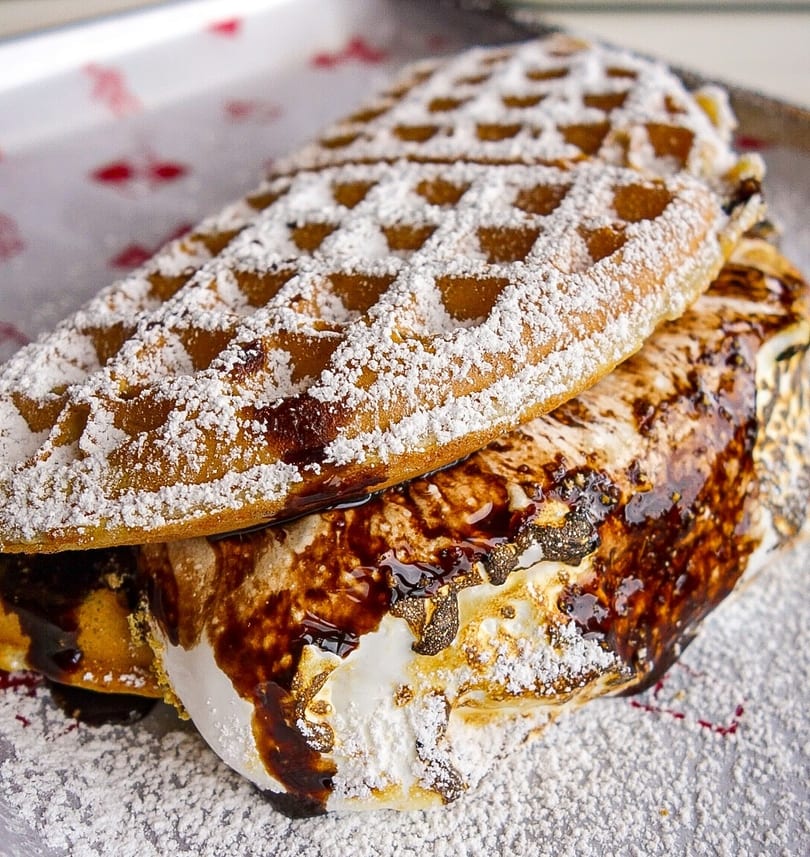 Golden waffle sandwich with gooey toasted marshmallow, chocolate drizzle, and powdered sugar.