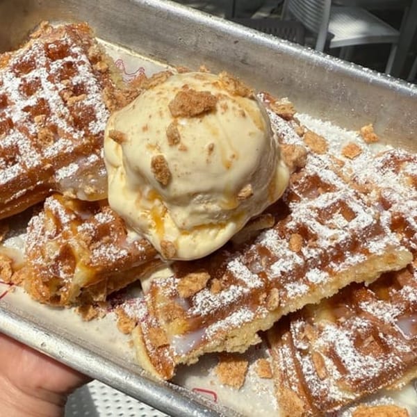 Waffles with powdered sugar, crumbled toppings, and a scoop of vanilla ice cream in a metal tray.