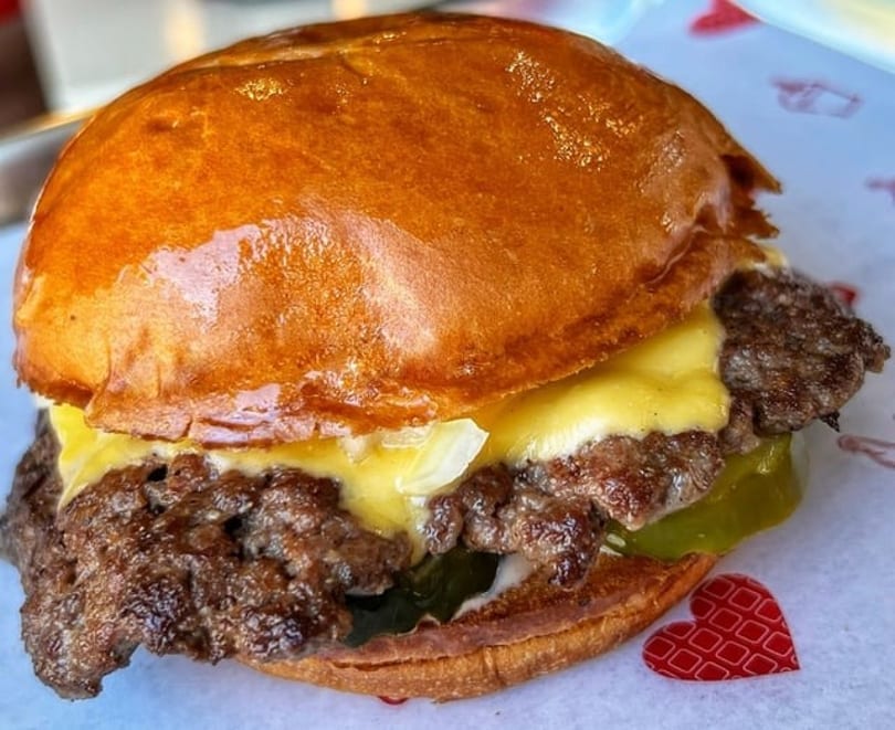 Close-up of a juicy cheeseburger with melted cheese, pickles, and a golden bun on patterned paper.